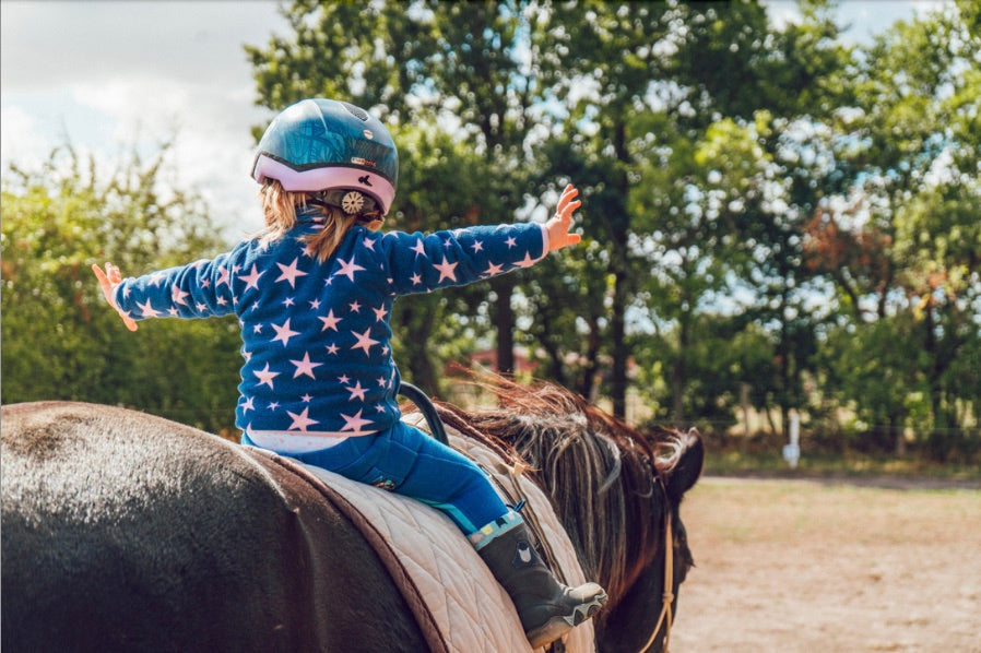 Kind reitet auf Pferd und streckt die Arme aus