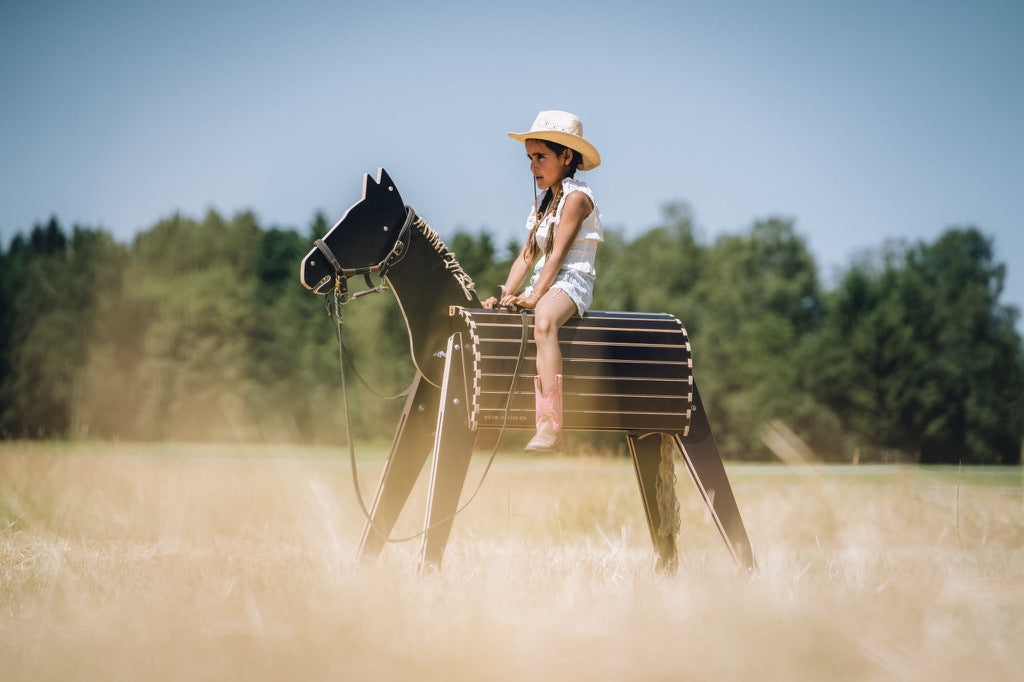 Kind reitet im wilden Westen Holzpferd mit Cowboy Hut und Reitstiefeln