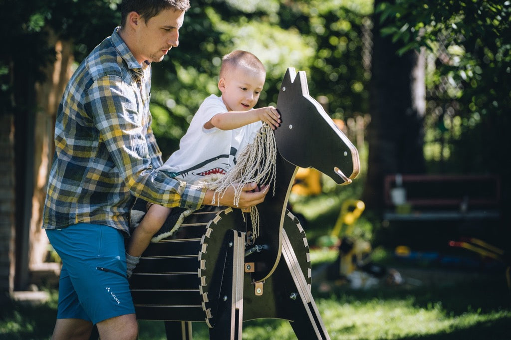 Kind reitet und spielt mit interaktivem Kopf von Holzpferd ferdi mit Vater